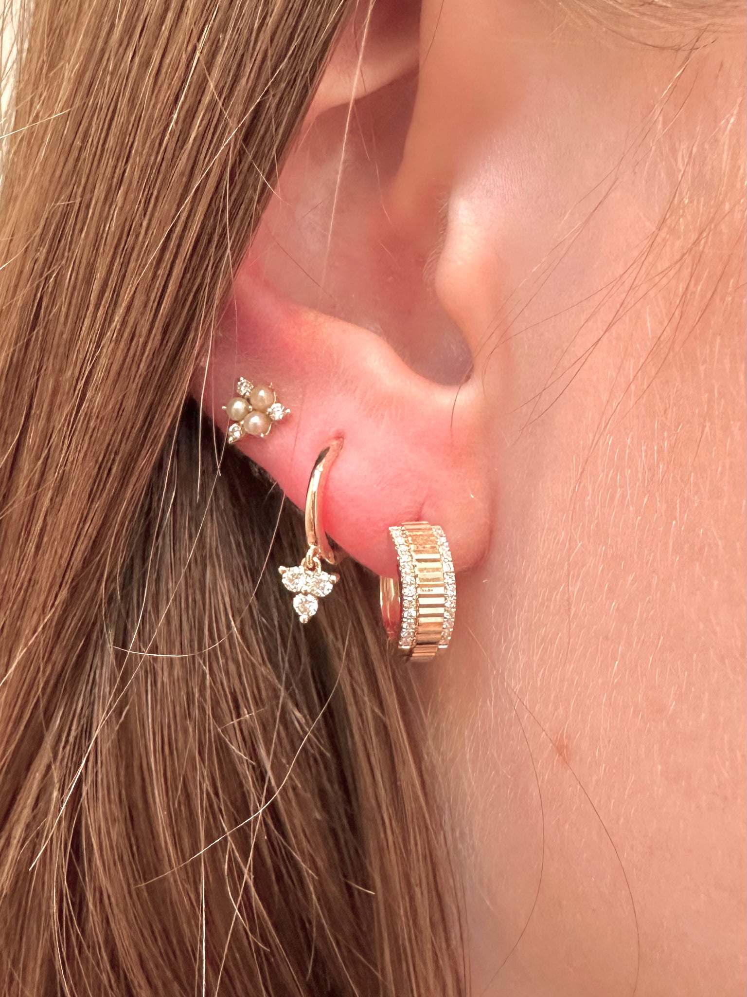Close-up of an ear wearing gold hoop earrings with pearl accents.